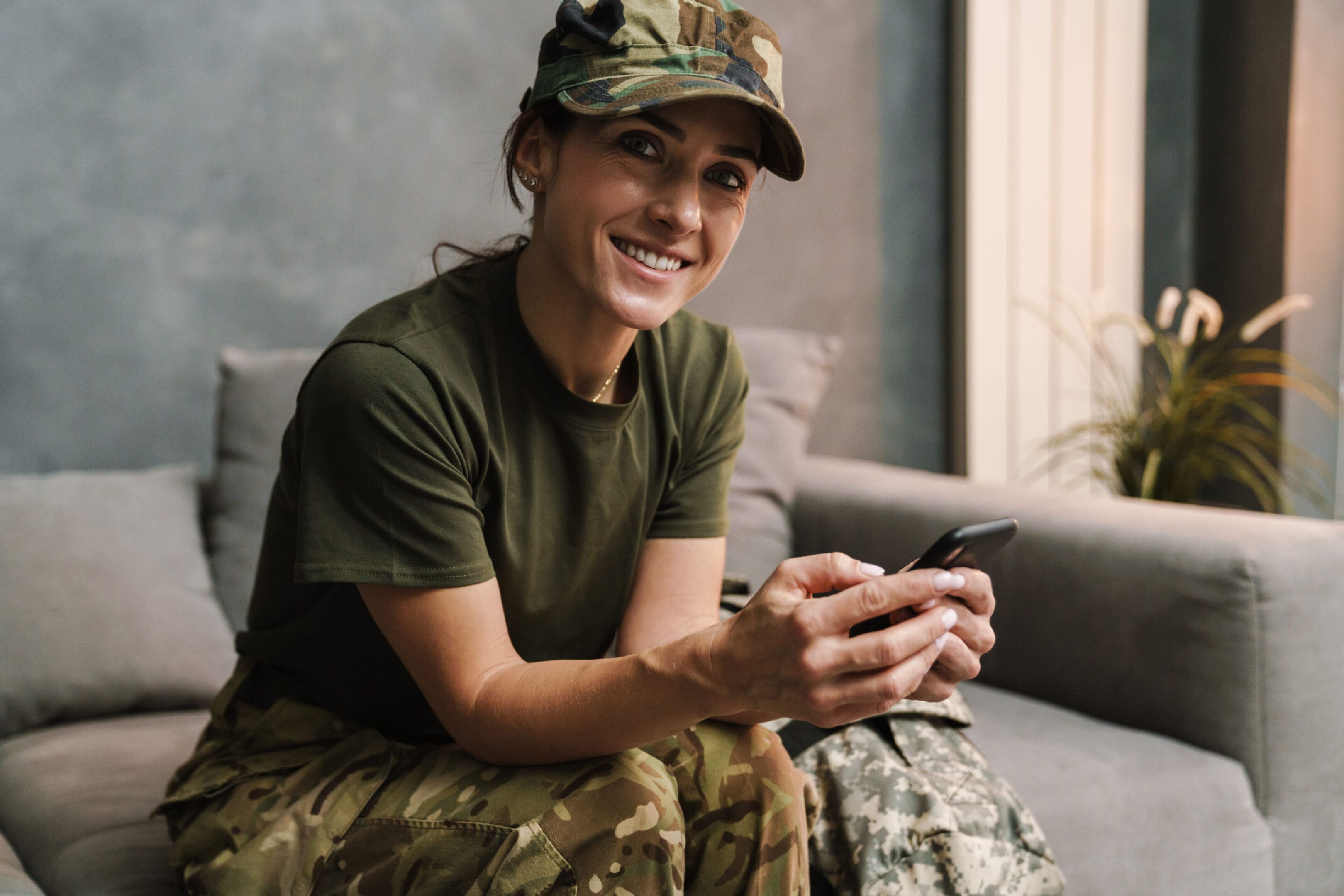 A woman in camouflage sitting on the couch holding her phone.