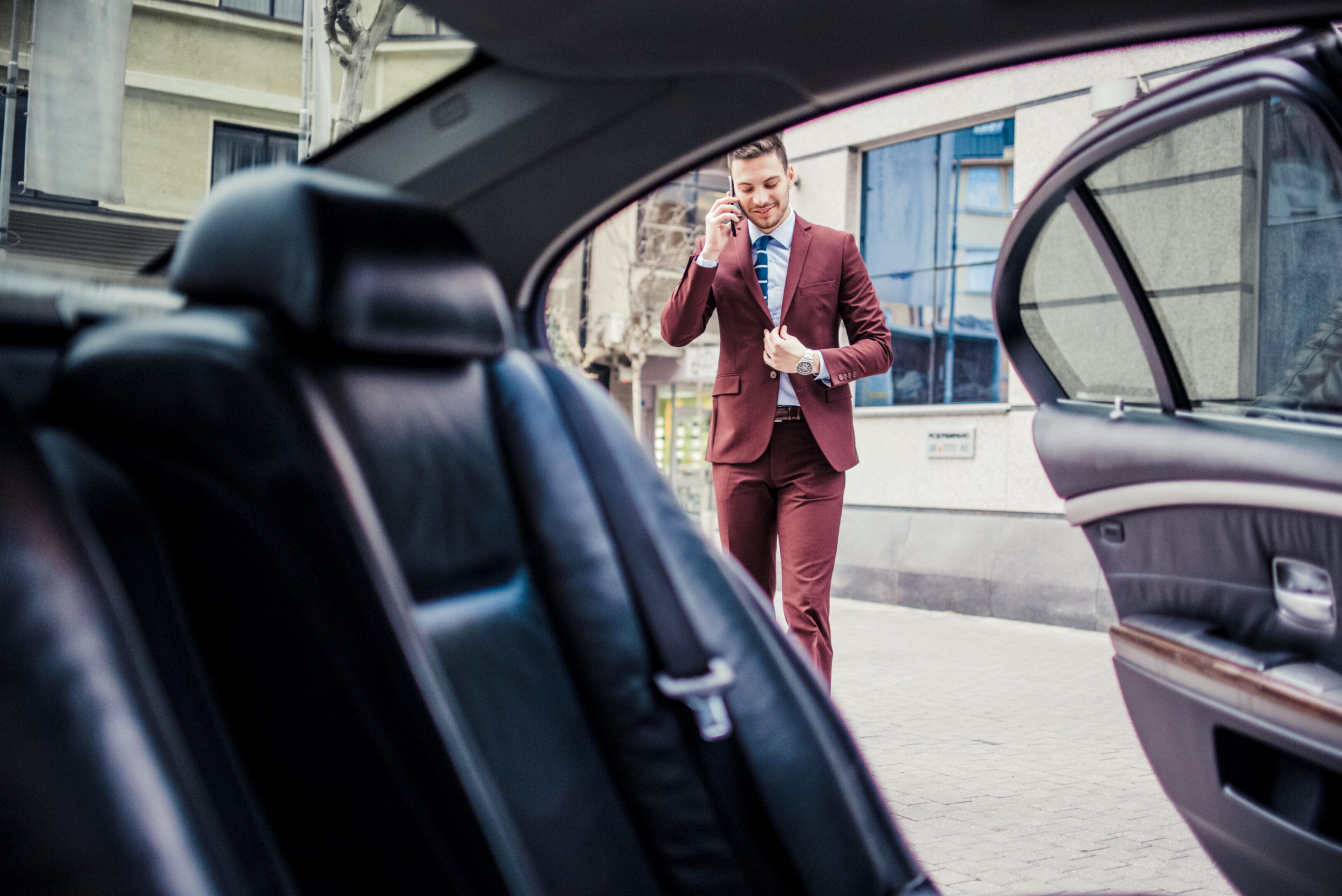 Young businessman standing next to his luxury car and talking on cell phone