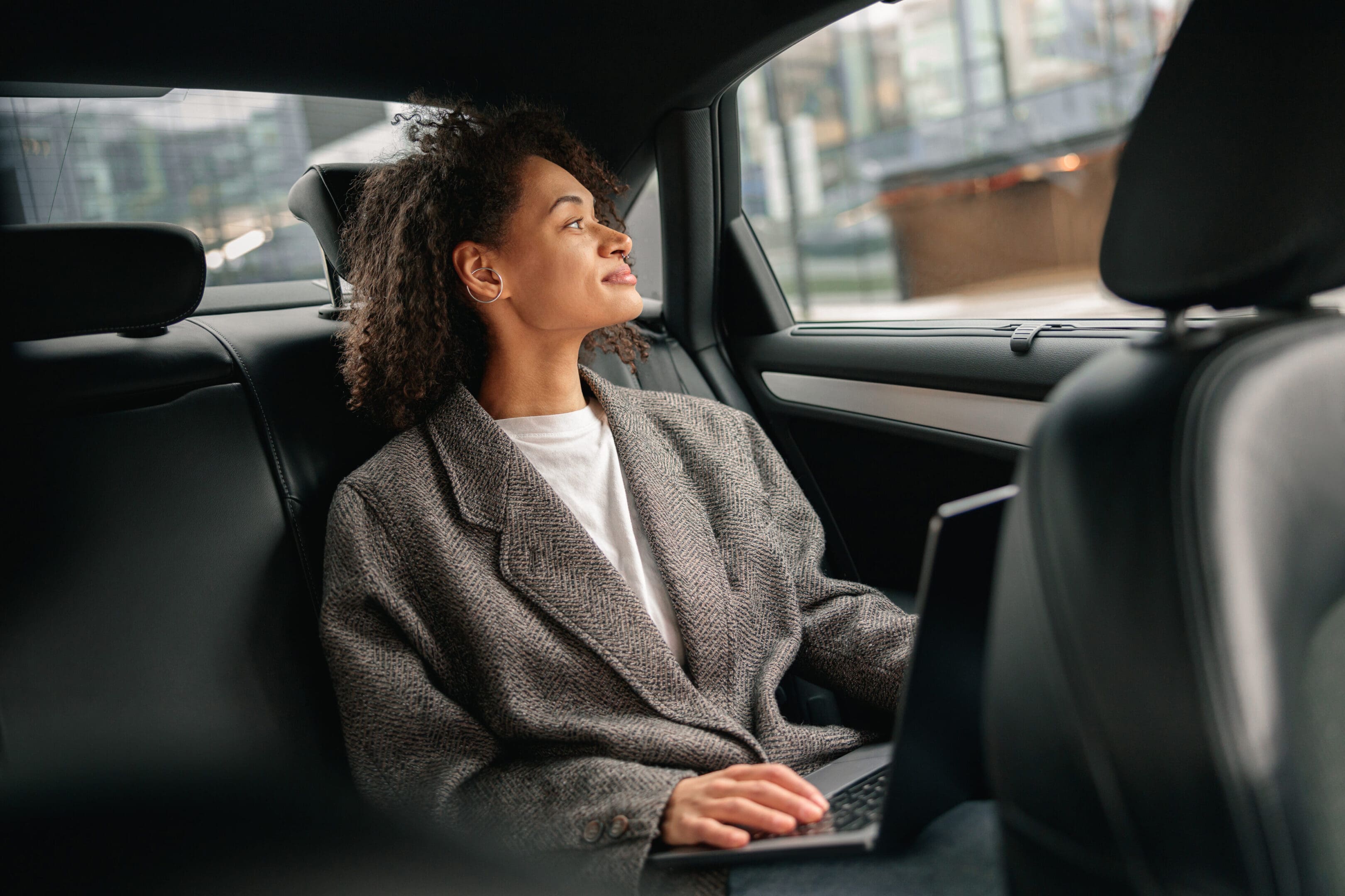 Woman manager working on laptop sitting car leather backseat on way to office. High quality photo